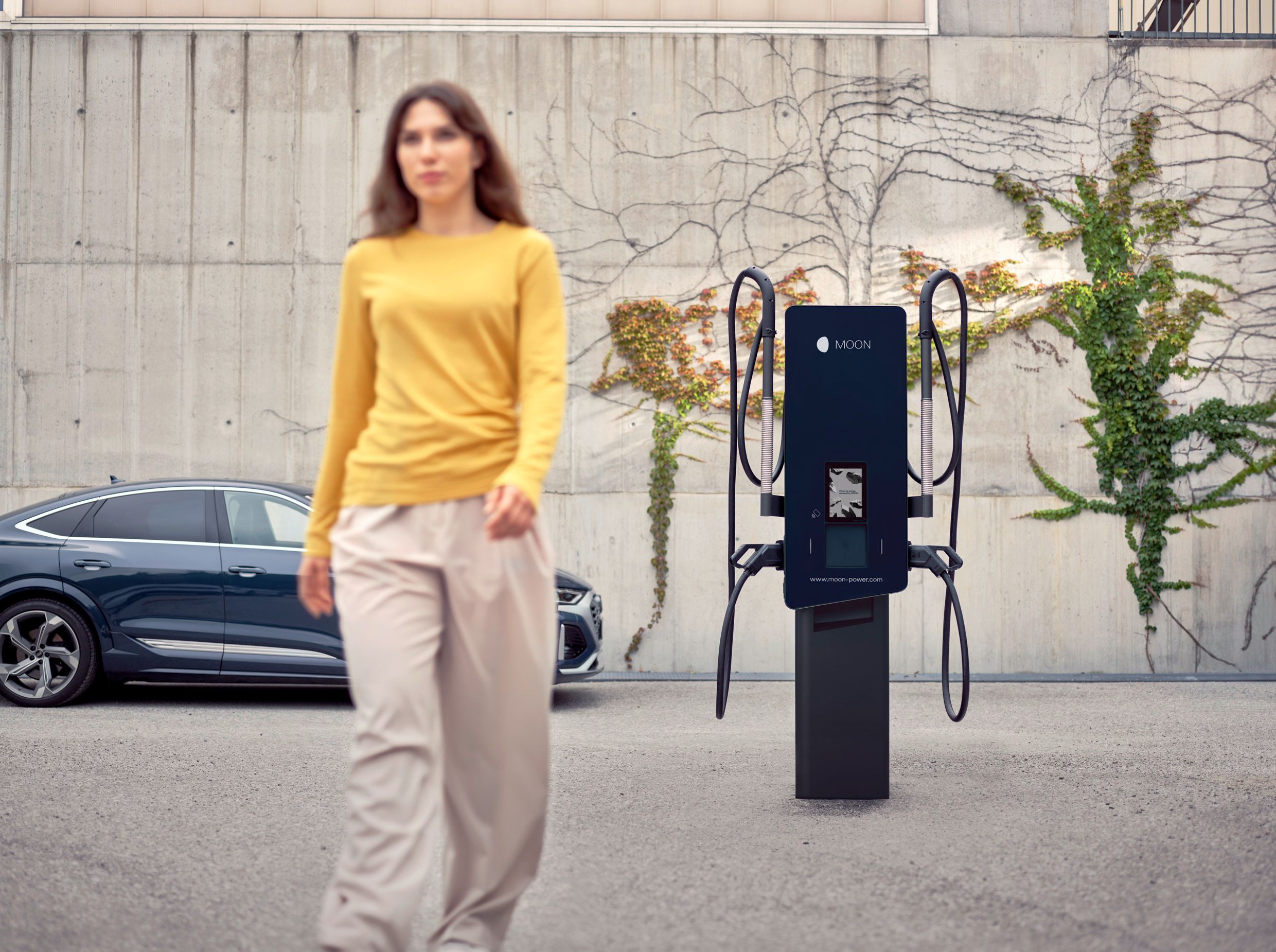 Femeie se îndepărtează de o stație de încărcare în fața unei mașini