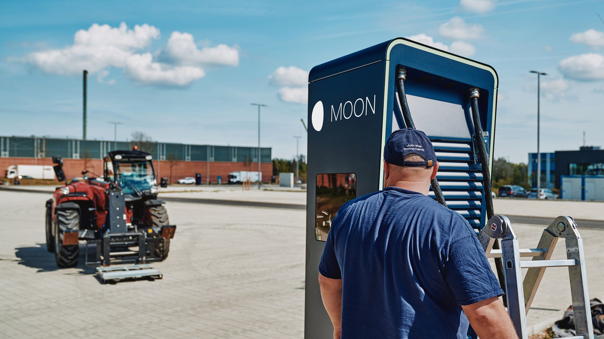 A man stands with a ladder in front of the POWER Charger fast charging station