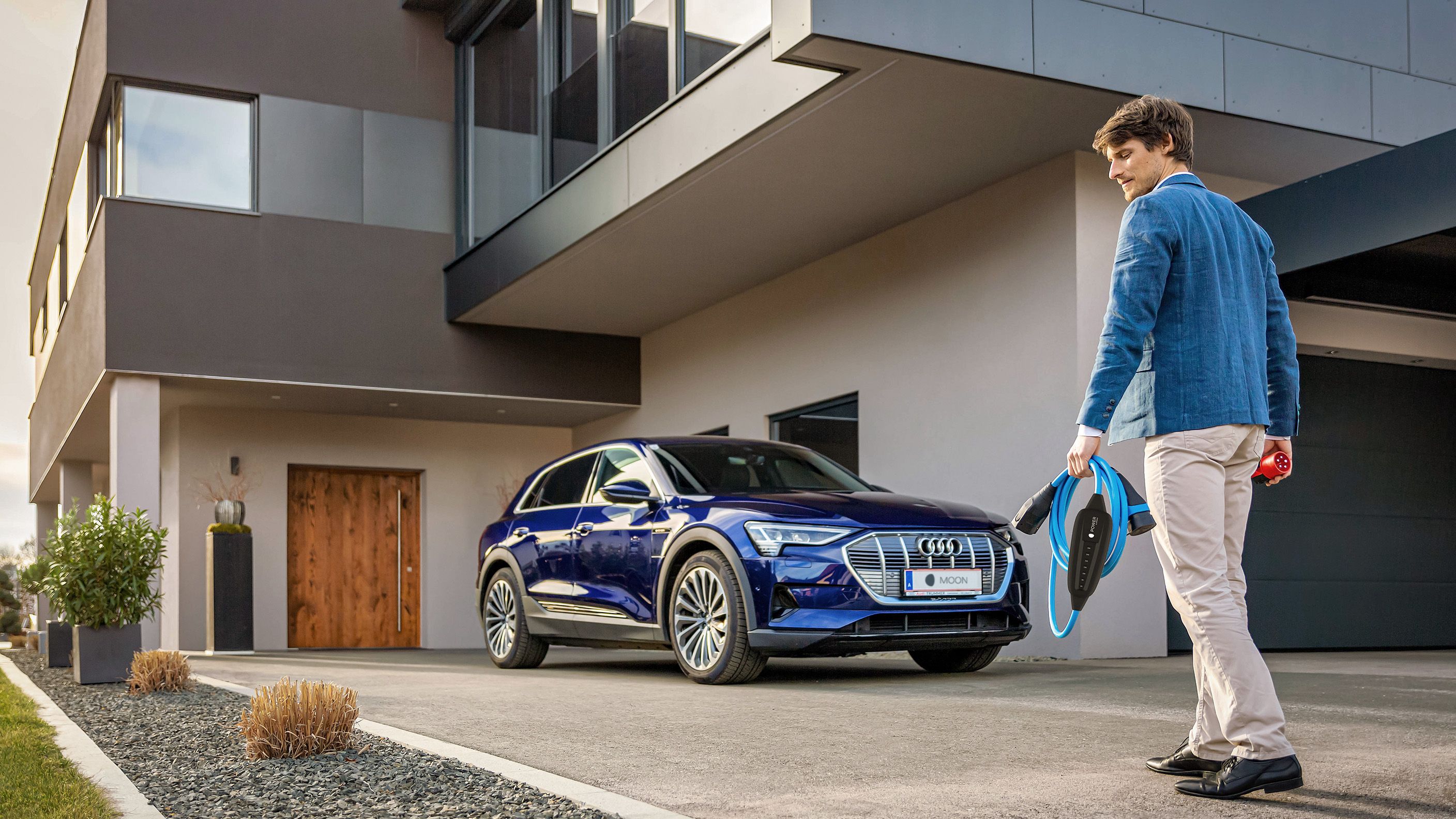 Bărbat merge spre o mașină lângă o casă cu un cablu în mână