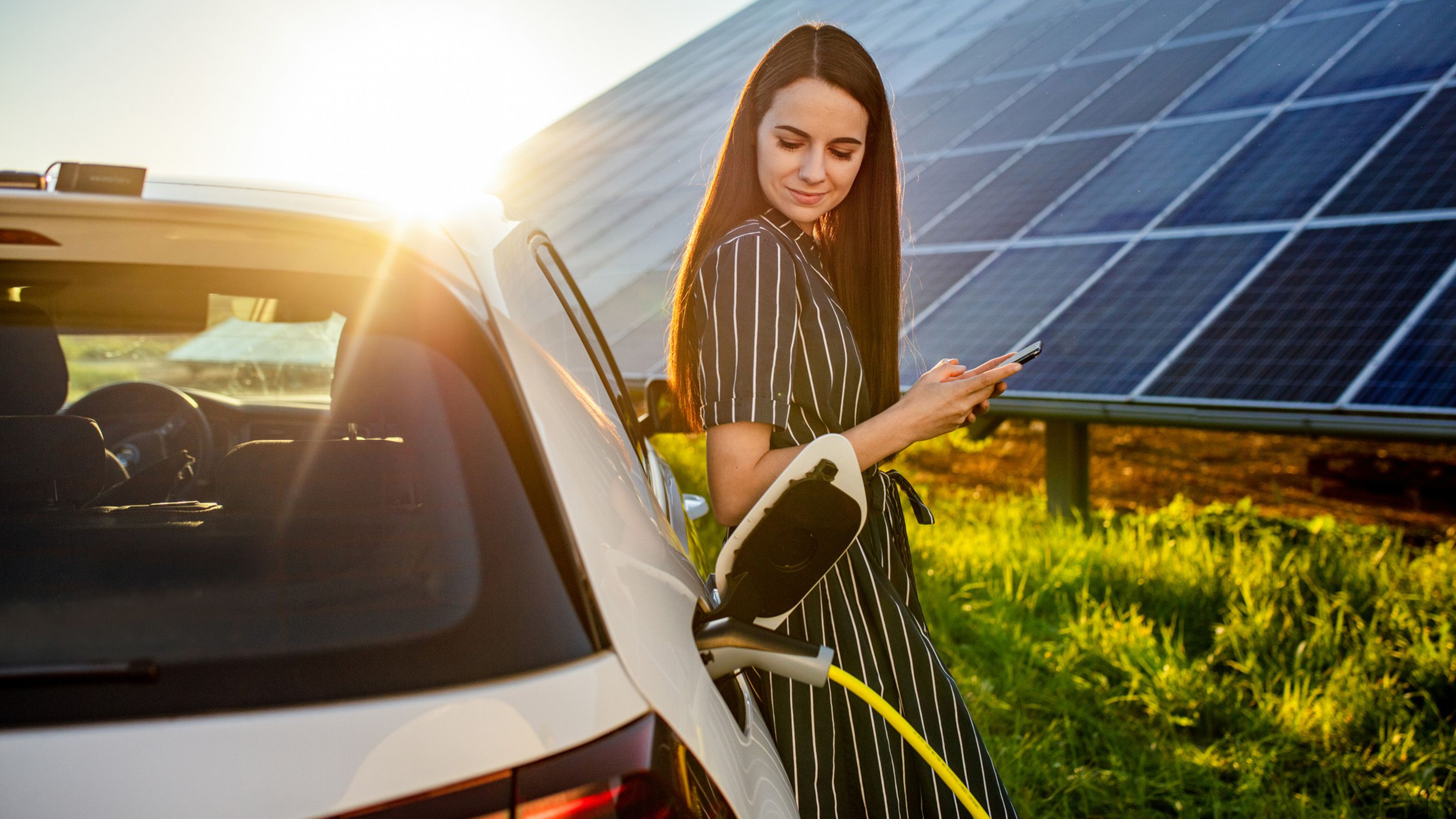 Femeie sprijinită de o mașină care se încarcă în fața unui sistem fotovoltaic
