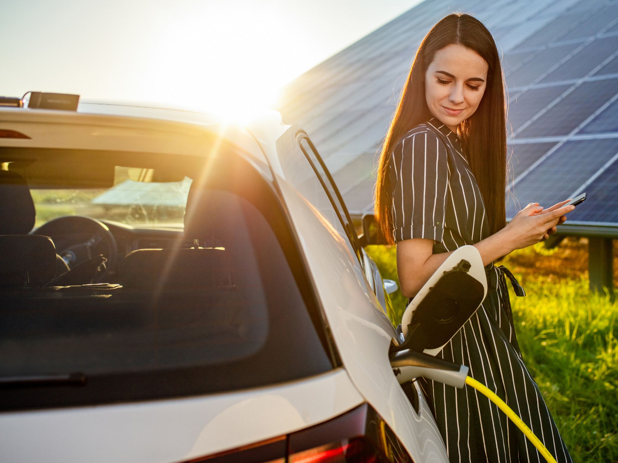Femeie sprijinită de o mașină care se încarcă în fața unui sistem fotovoltaic