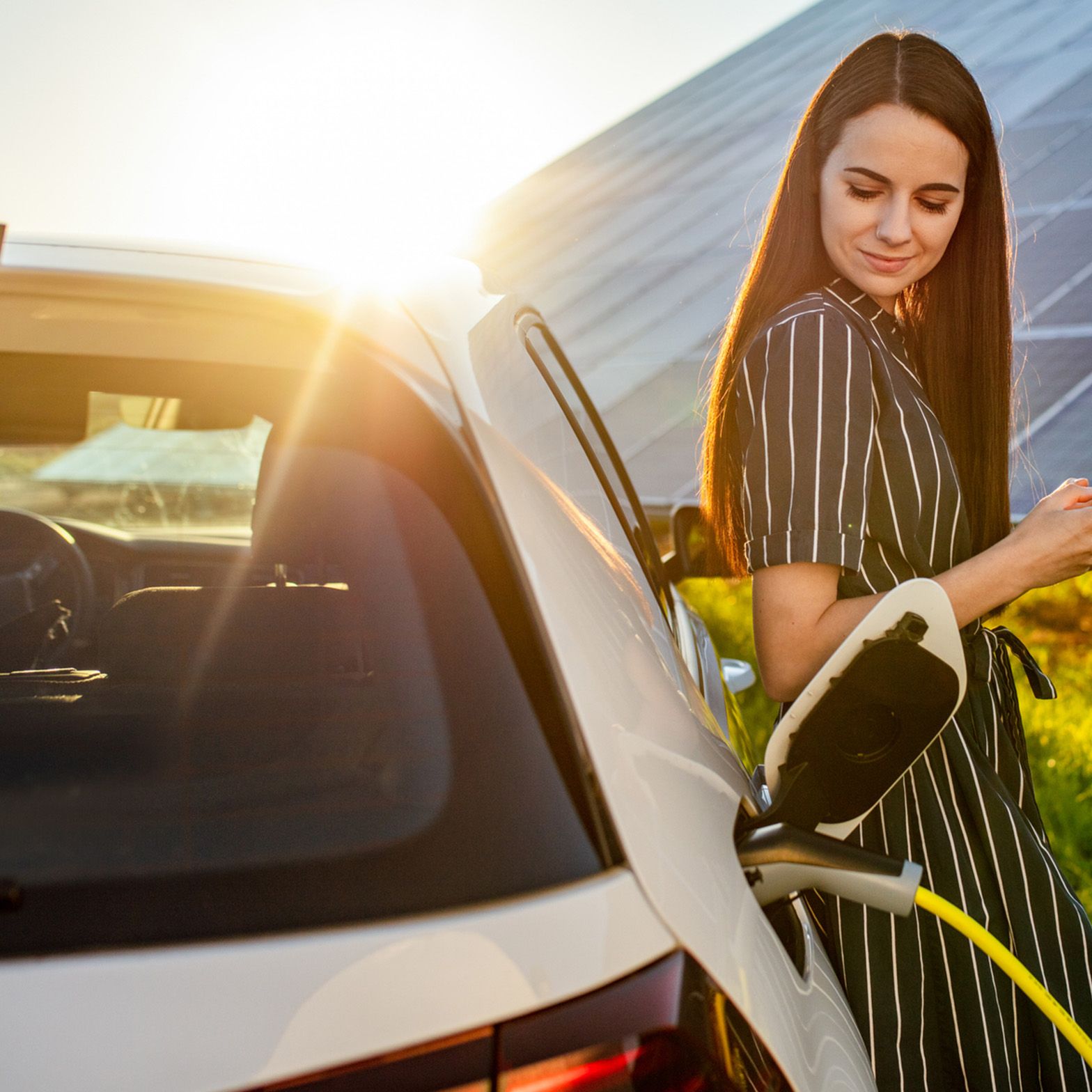 Femeie sprijinită de o mașină care se încarcă în fața unui sistem fotovoltaic