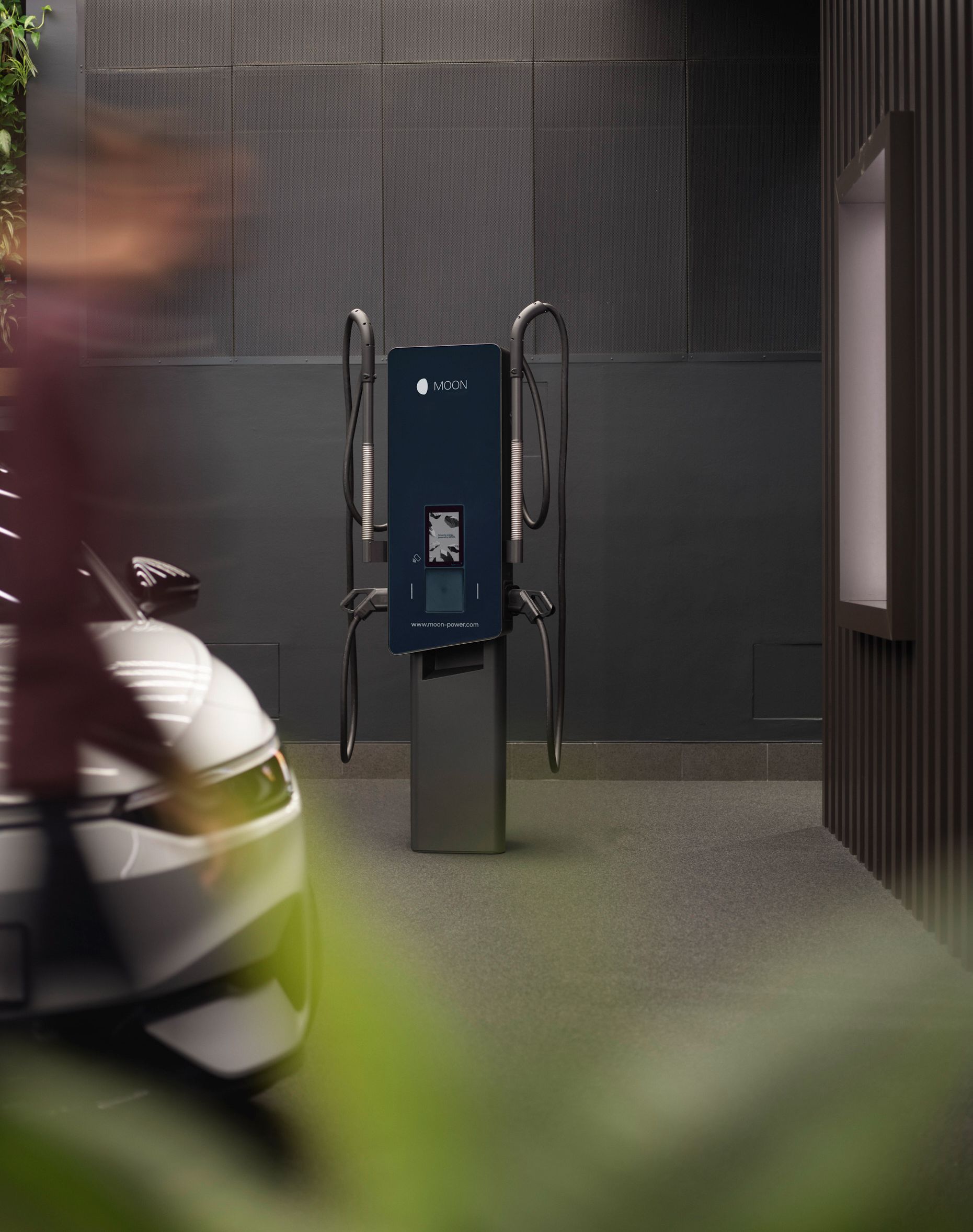 Stația de încărcare în fața unui perete gri cu mașina în prim-plan