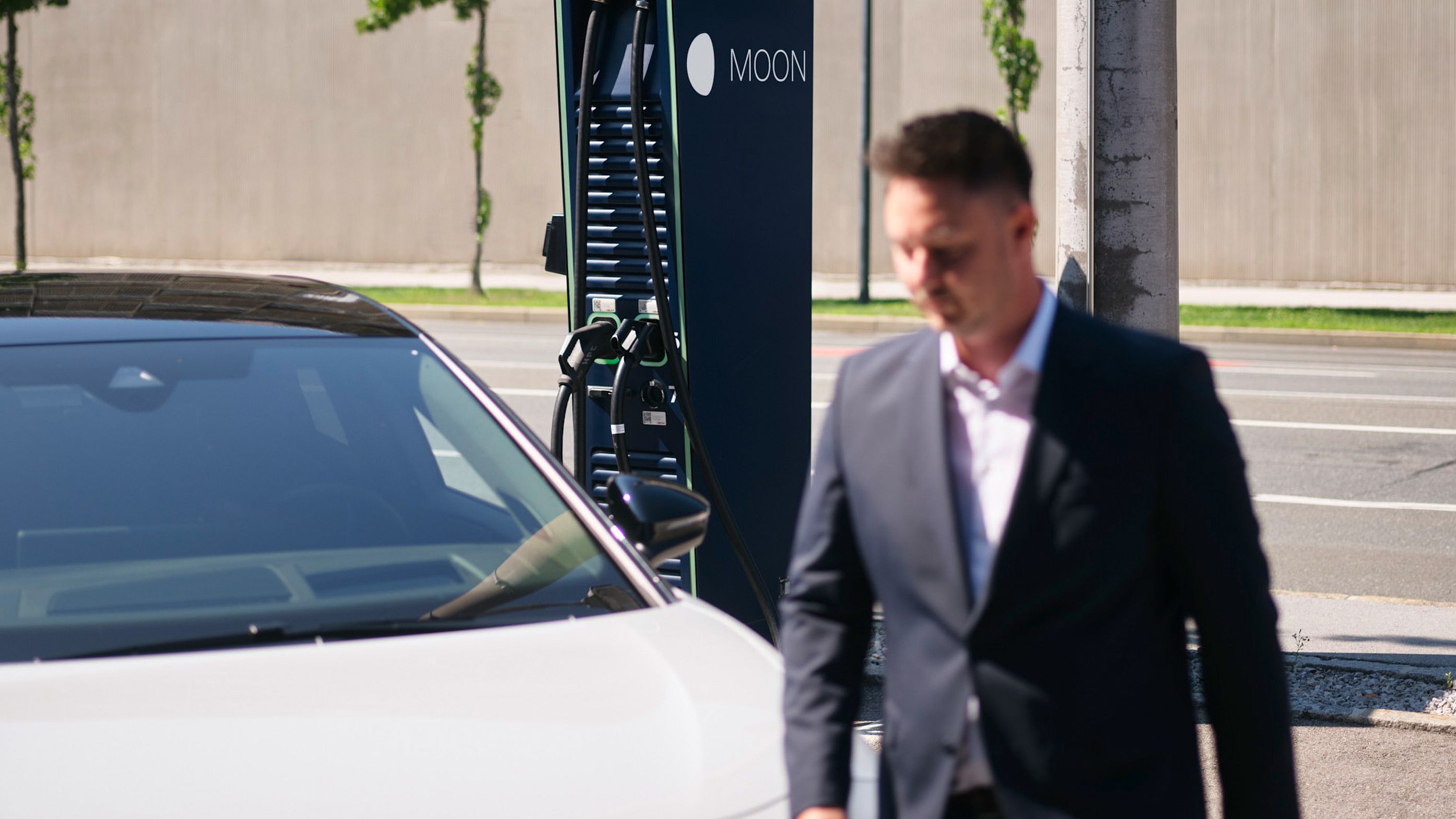 Bărbat merge în fața unei mașini în fața unei stații de încărcare