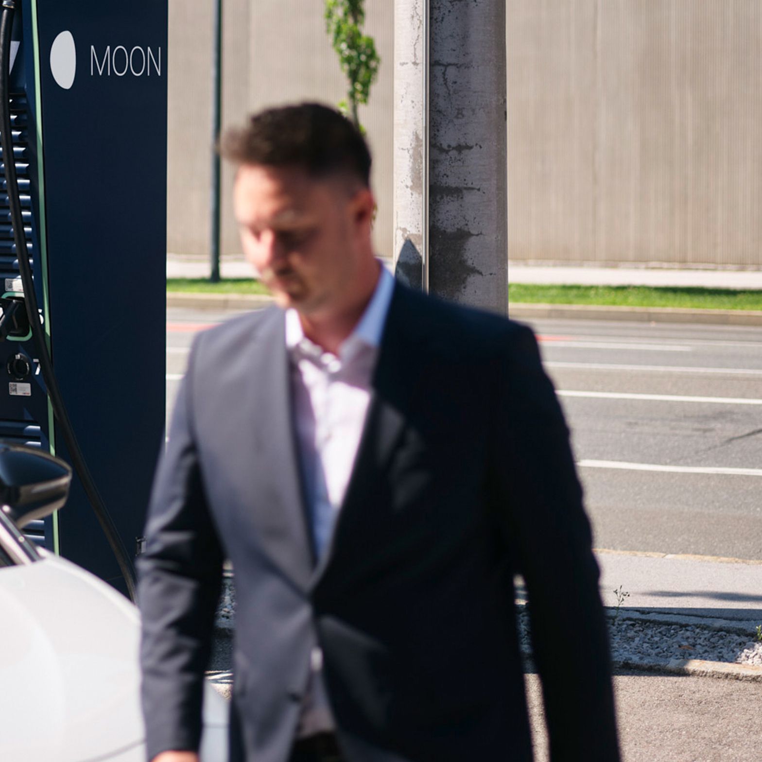 Bărbat merge în fața unei mașini în fața unei stații de încărcare